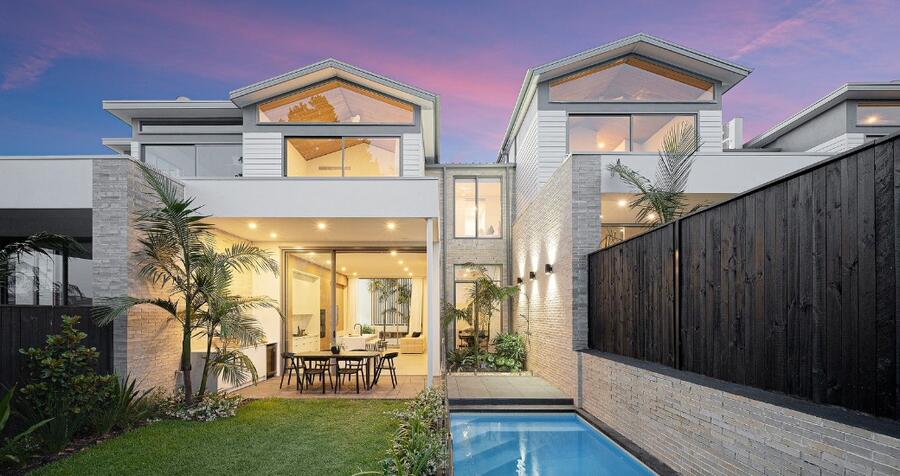 Twilight rear elevation of the two-storey Balgowlah townhouse, gabled roofline glowing warm against a dusk sky, with the alfresco dining area and lap pool in the foreground.