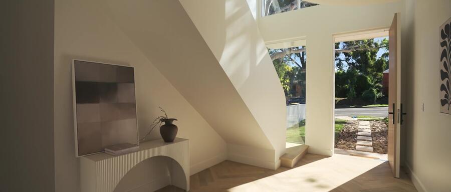 Sculptural curved entry hall with herringbone oak flooring and floor-to-ceiling glazing, open front door framing a stone garden path