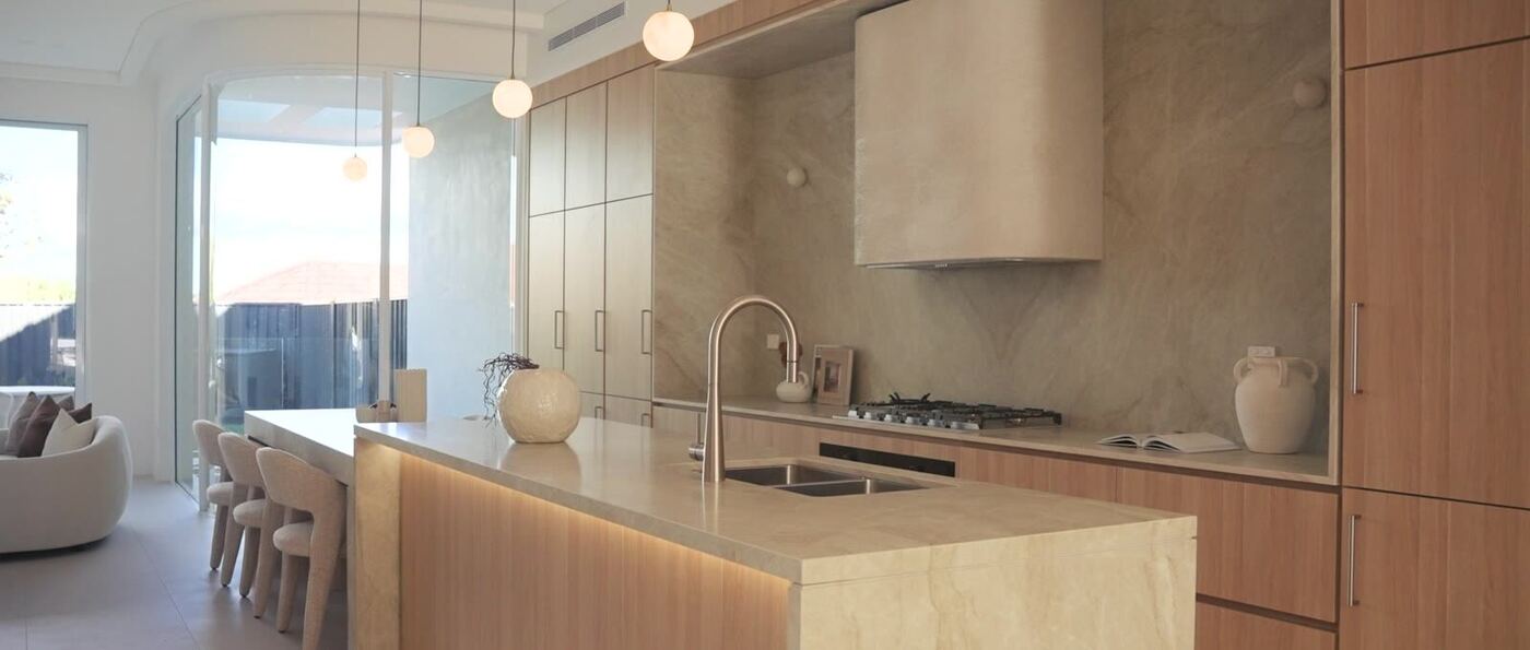Open-plan kitchen with book-matched stone splashback, timber cabinetry and waterfall-edge island, opening through to the dining and living areas