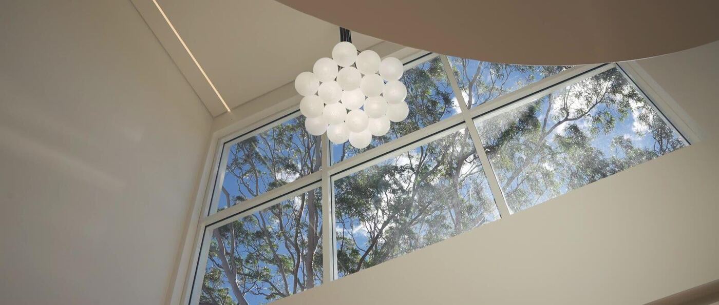 Spherical glass pendant light beneath the home’s curved double-height ceiling, framed by full-height windows onto the tree canopy