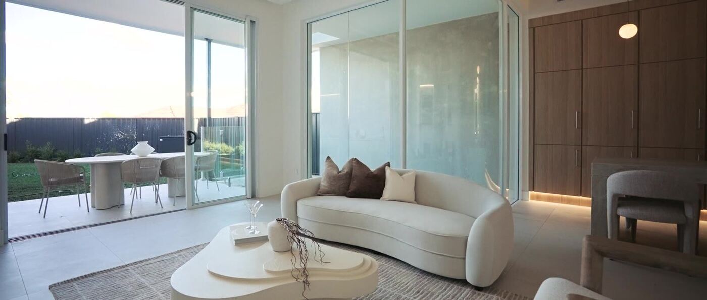 Living area with a curved boucle sofa and timber joinery, glass sliding doors opening onto the outdoor dining terrace