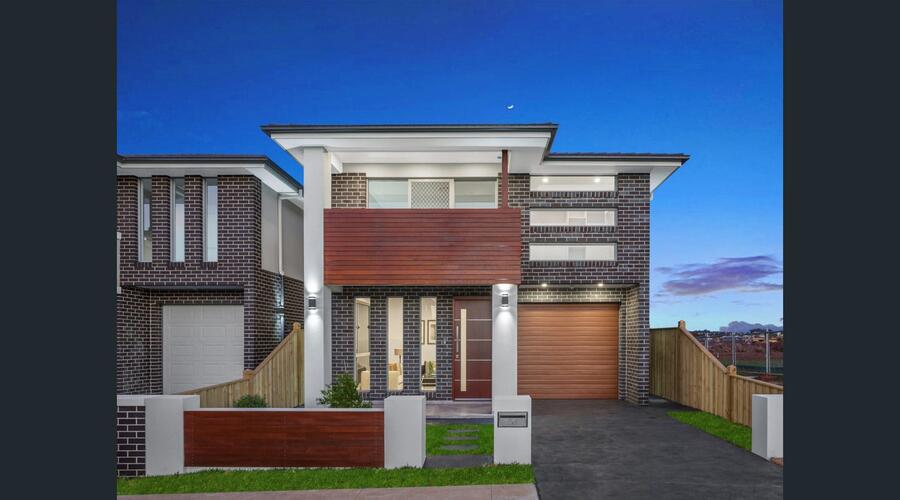 Twilight view of the two-storey brick facade home with timber-look garage door and cantilevered timber-slat balcony, Oran Park