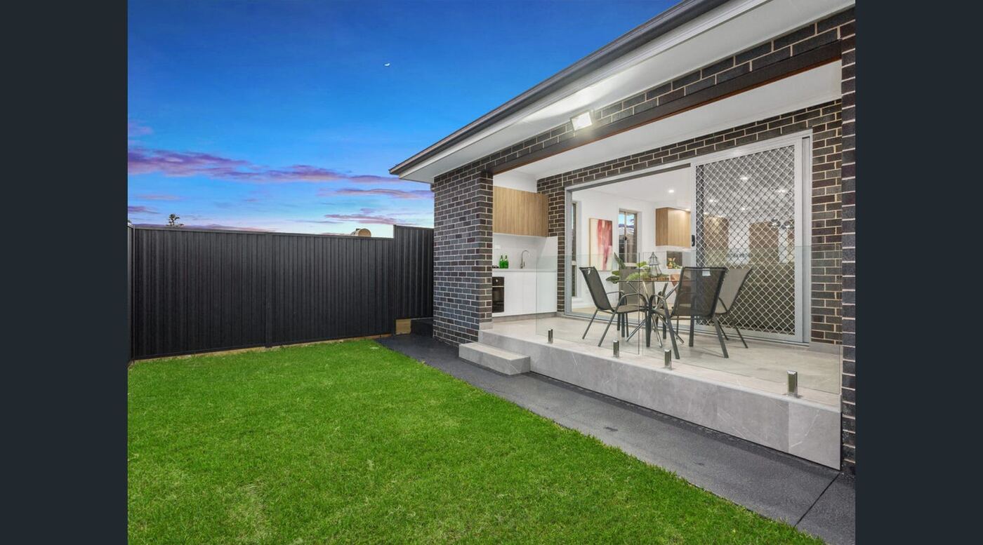 Alfresco entertaining area with built-in outdoor kitchen and dining setting opening onto the rear lawn at dusk
