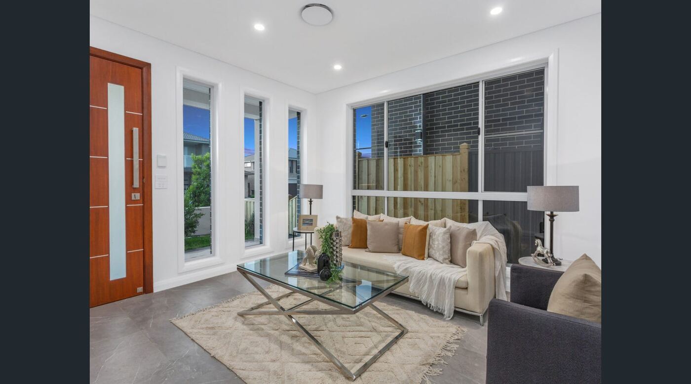 Living room with floor-to-ceiling windows, glass coffee table and neutral furnishings beside the front entry