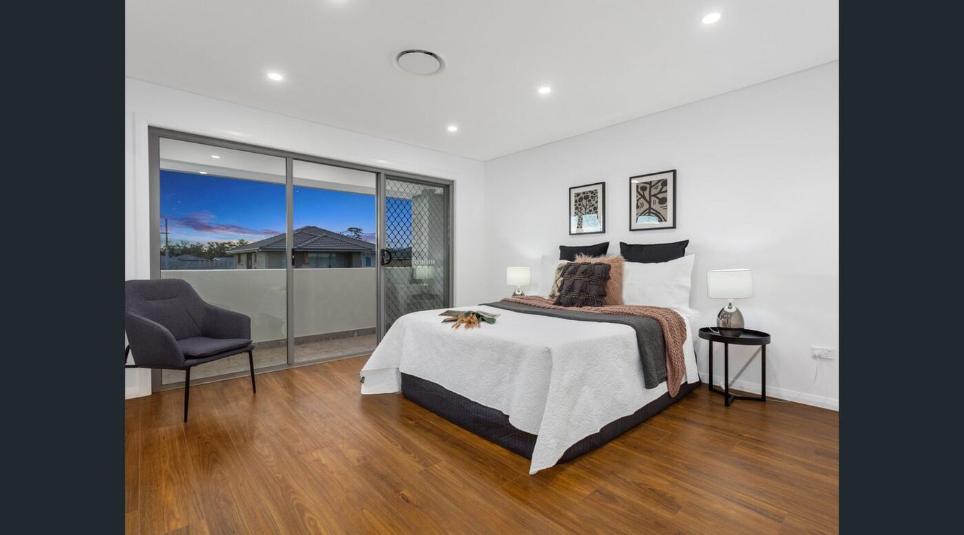 Main bedroom with timber flooring, private balcony access and a dusk view over the neighbourhood