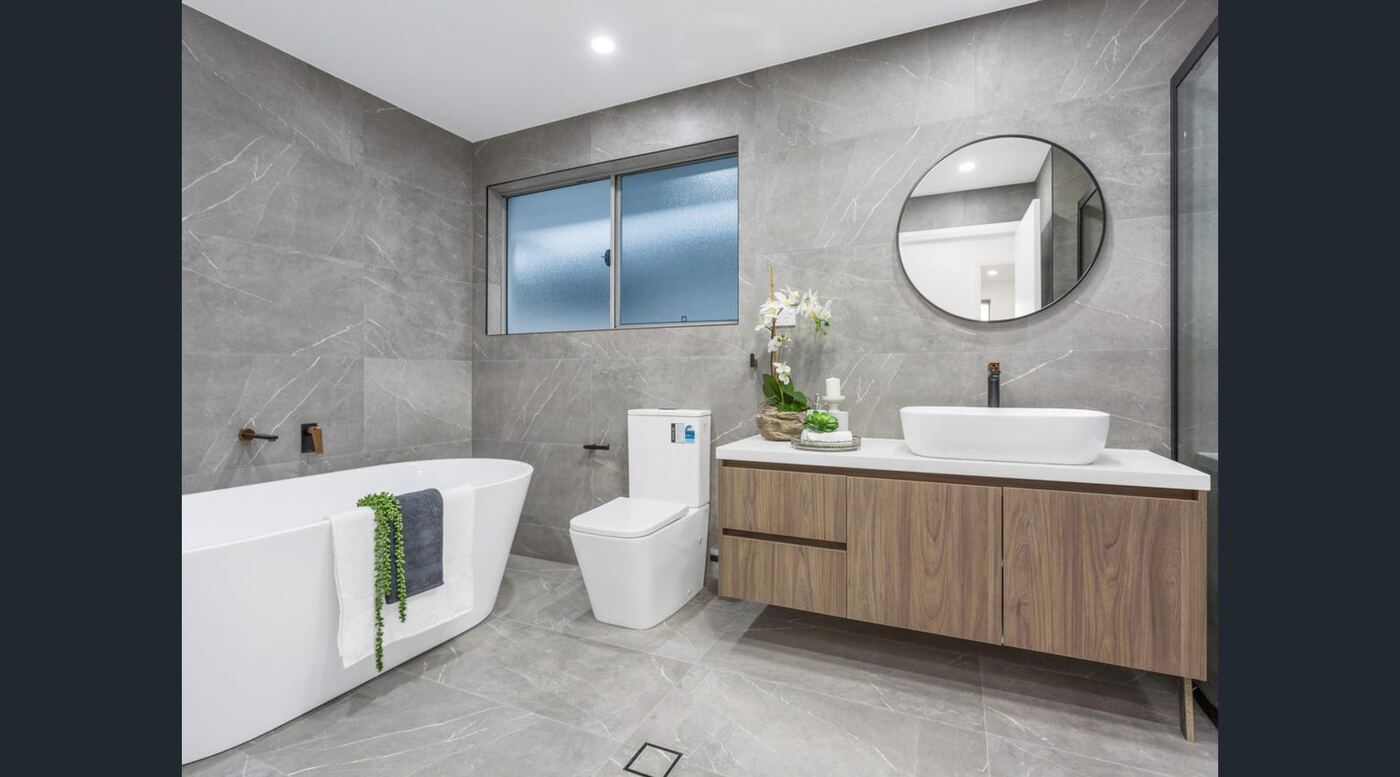 Bathroom with freestanding soaking tub, full-height stone-look tiling and round mirror