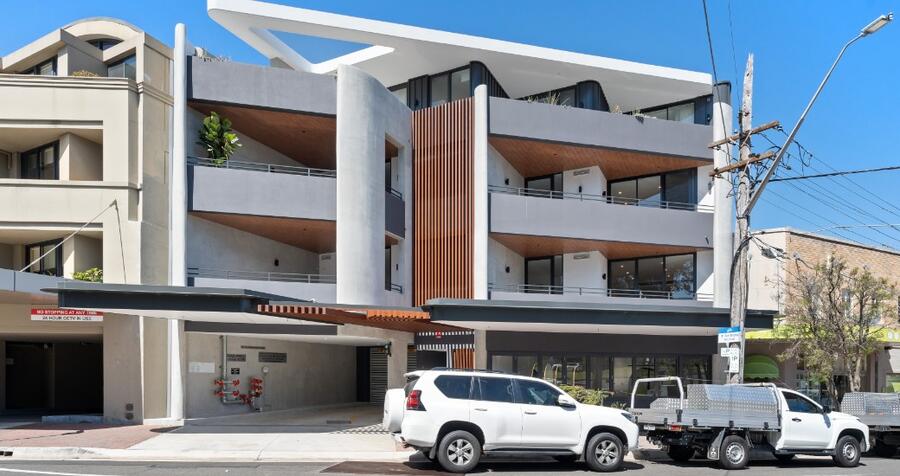 Front facade of the completed Seaforth building, showing the sculptural white canopy roof, curved off-form concrete forms and timber batten screen at street level.