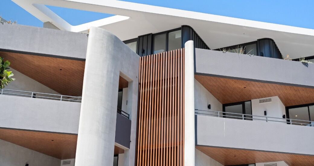 Close-up of the building’s facade detailing, showing curved off-form concrete columns and a vertical timber batten screen.