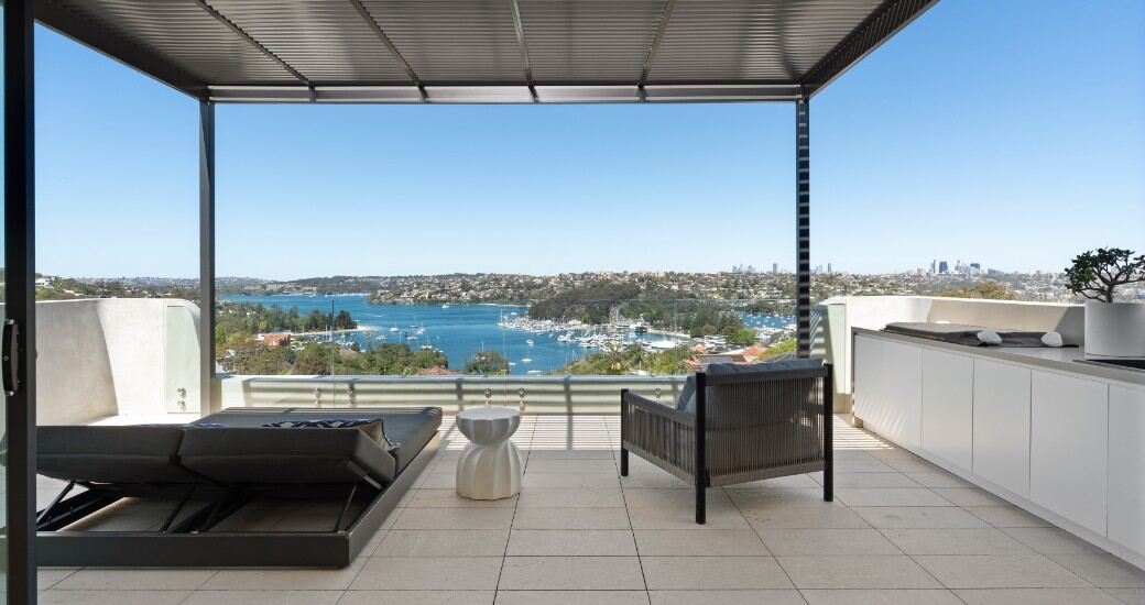 Rooftop terrace with outdoor lounge seating and kitchenette, overlooking Middle Harbour and the Sydney city skyline.