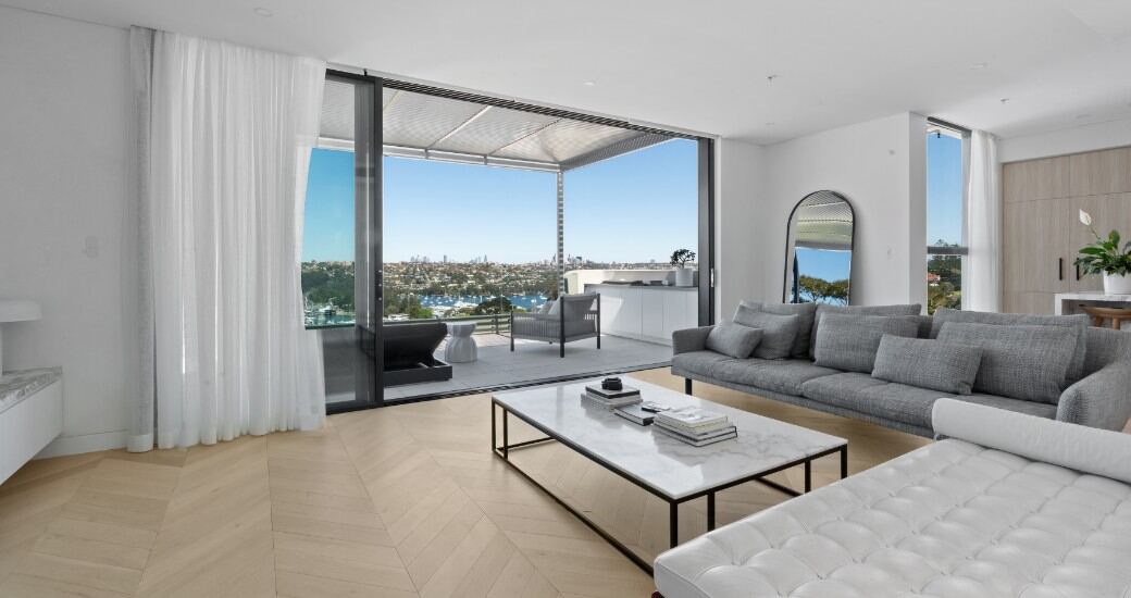 Open-plan living room with chevron oak flooring, opening through glass sliding doors to a terrace with harbour views.