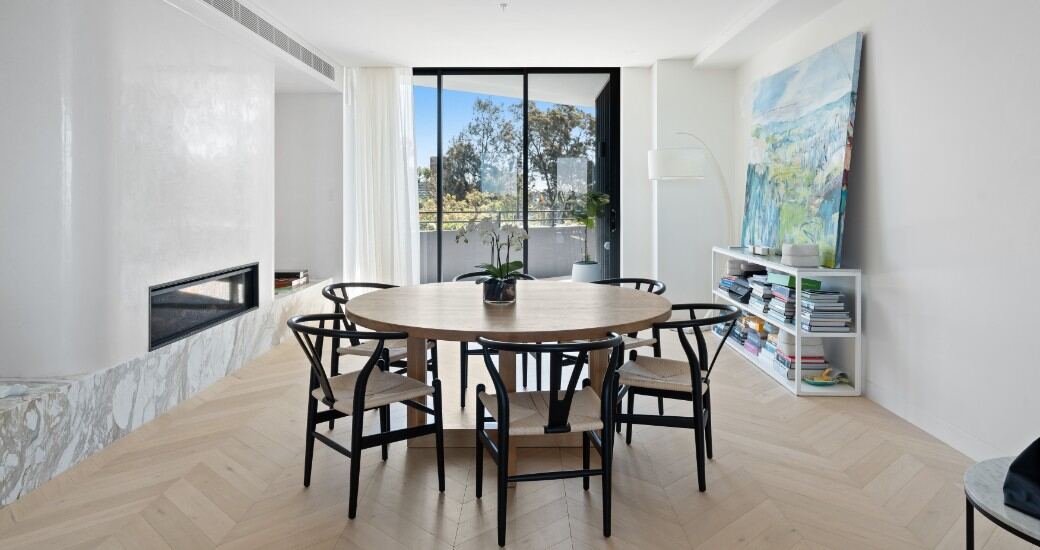 Dining area with a round timber table, black wishbone chairs, a gas fireplace and marble hearth.