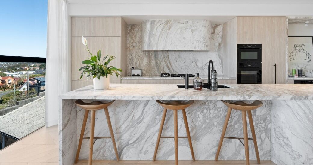 Kitchen with a full-height marble waterfall island, integrated oak joinery and gas cooktop.