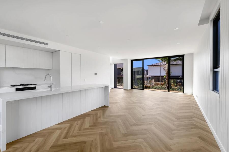 Open-plan kitchen and living area with herringbone timber flooring opening onto a landscaped courtyard through full-height black-framed sliding doors