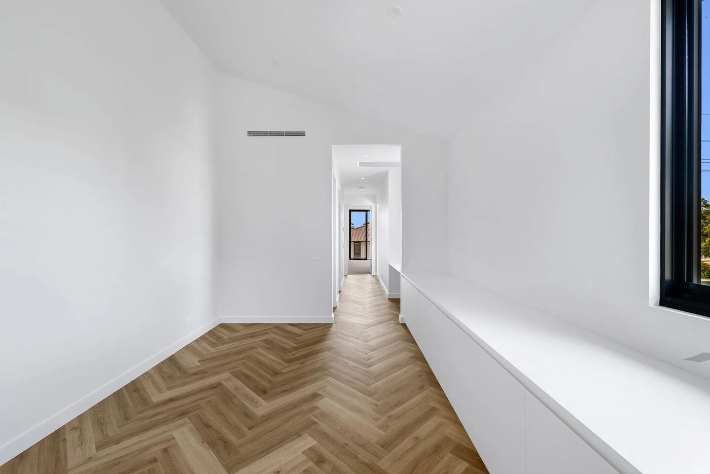 Vaulted hallway with herringbone timber flooring and a built-in window seat leading toward a bedroom with a street view