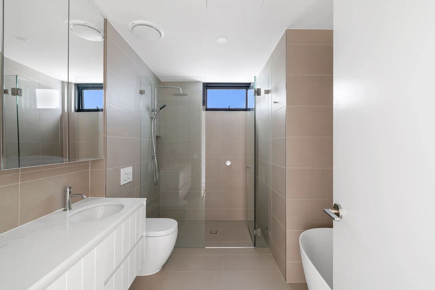 Ensuite bathroom with frameless glass shower, freestanding bathtub, floating stone-top vanity and full-height mirror